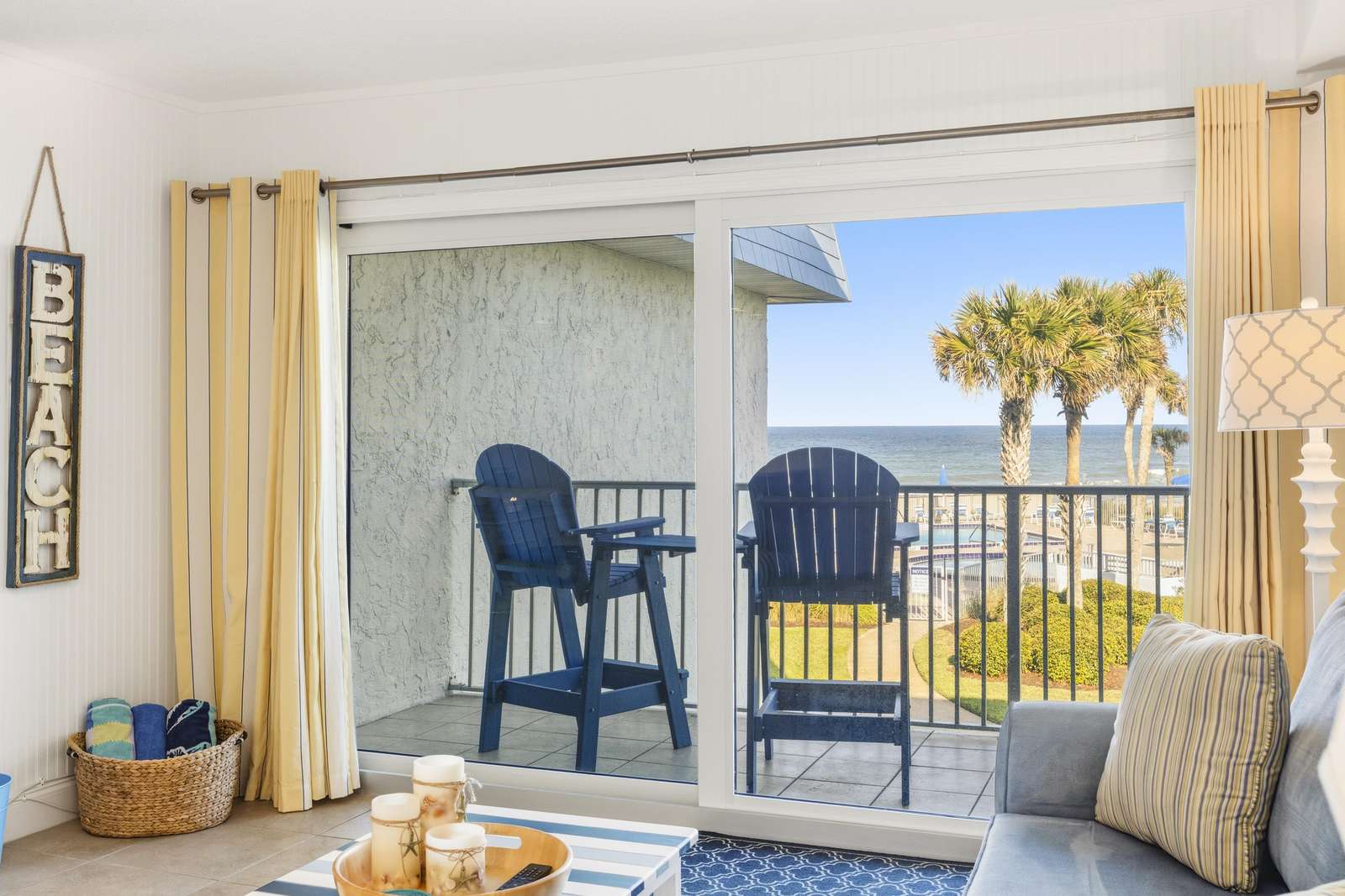 Sliding glass doors open to a balcony with navy Adirondack chairs overlooking palm trees and ocean views. - property