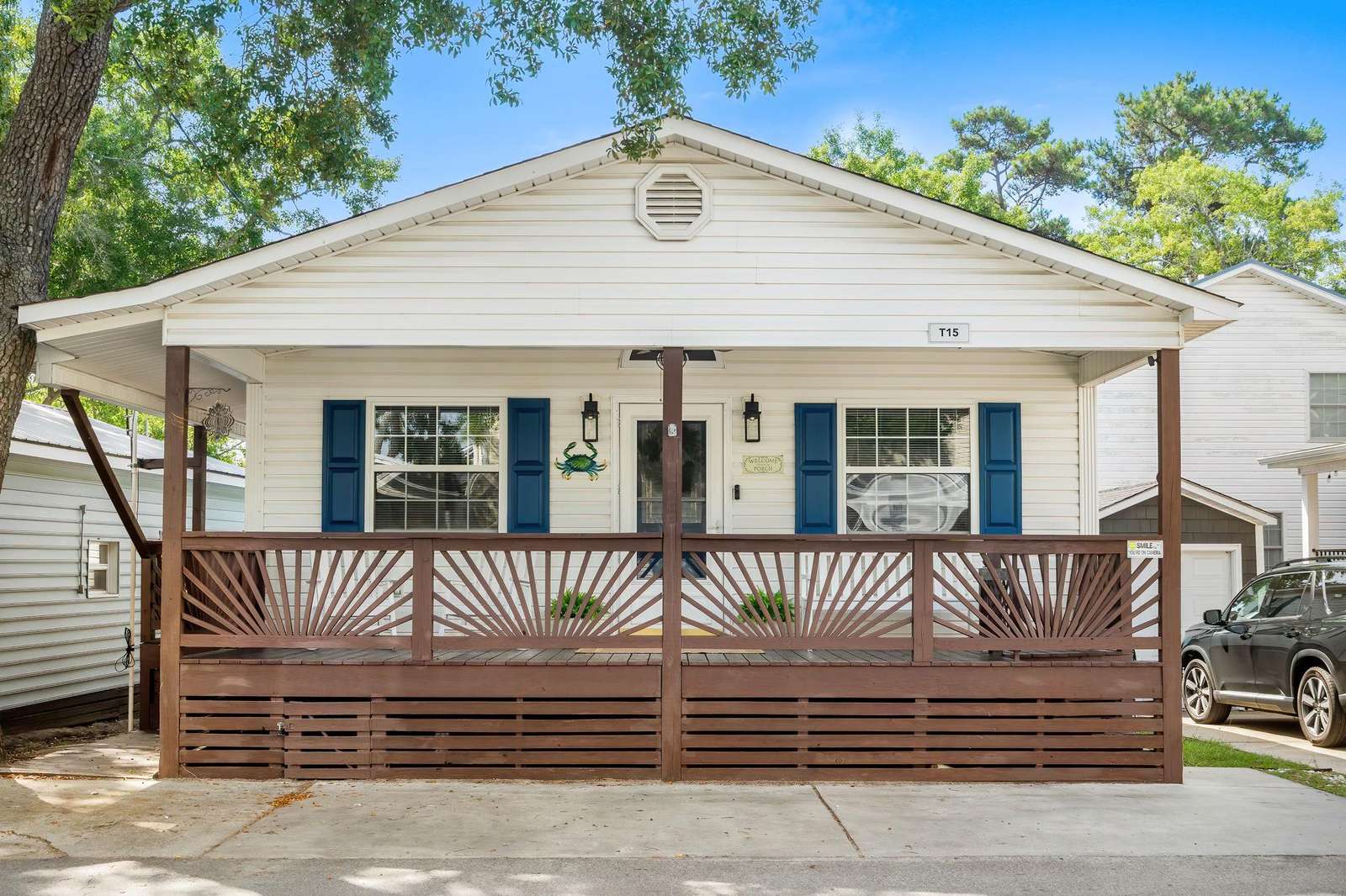 Front porch with decorative wooden railing, white siding, blue window shutters, and a central entry door. - property