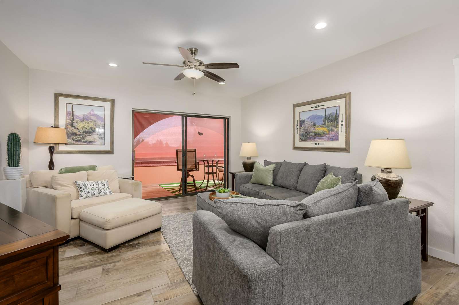 Living room with wood-look tile flooring, gray and beige sofas, Southwestern artwork, and sliding glass doors to balcony. - property