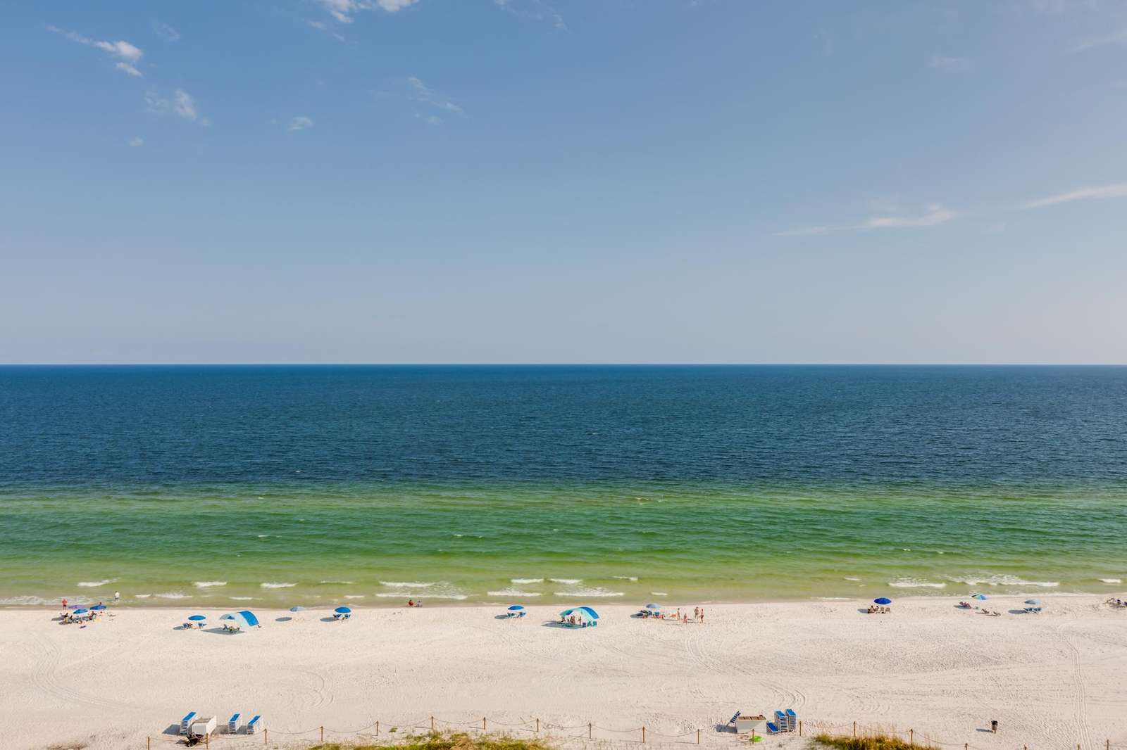 Wide view of the white sandy beach and calm green-blue Gulf waters under a clear blue sky. - property