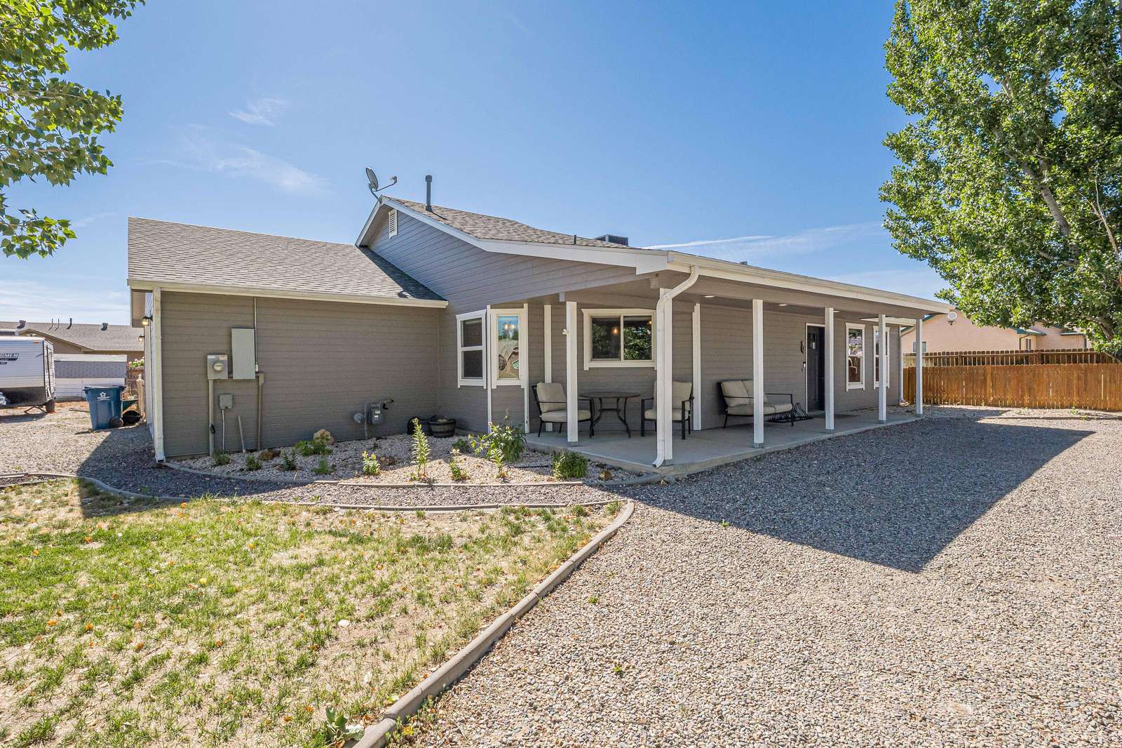 Covered patio with cushioned chairs and a glass-top table overlooks a gravel yard and partial lawn. - property