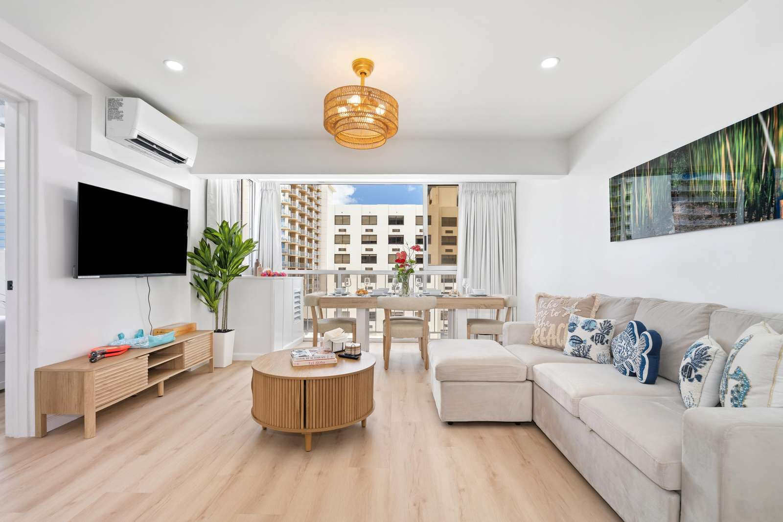 A beige sectional couch adorned with patterned pillows faces a wall-mounted TV above a slatted wood media cabinet.