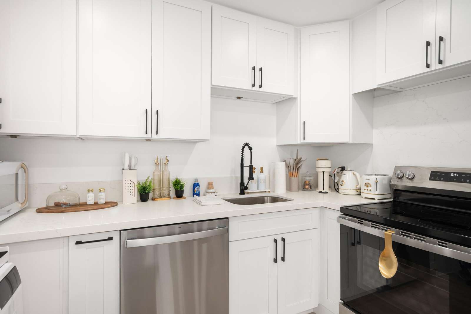 L-shaped kitchen countertop with white quartz, black faucet, stainless steel dishwasher, and stainless electric stove.