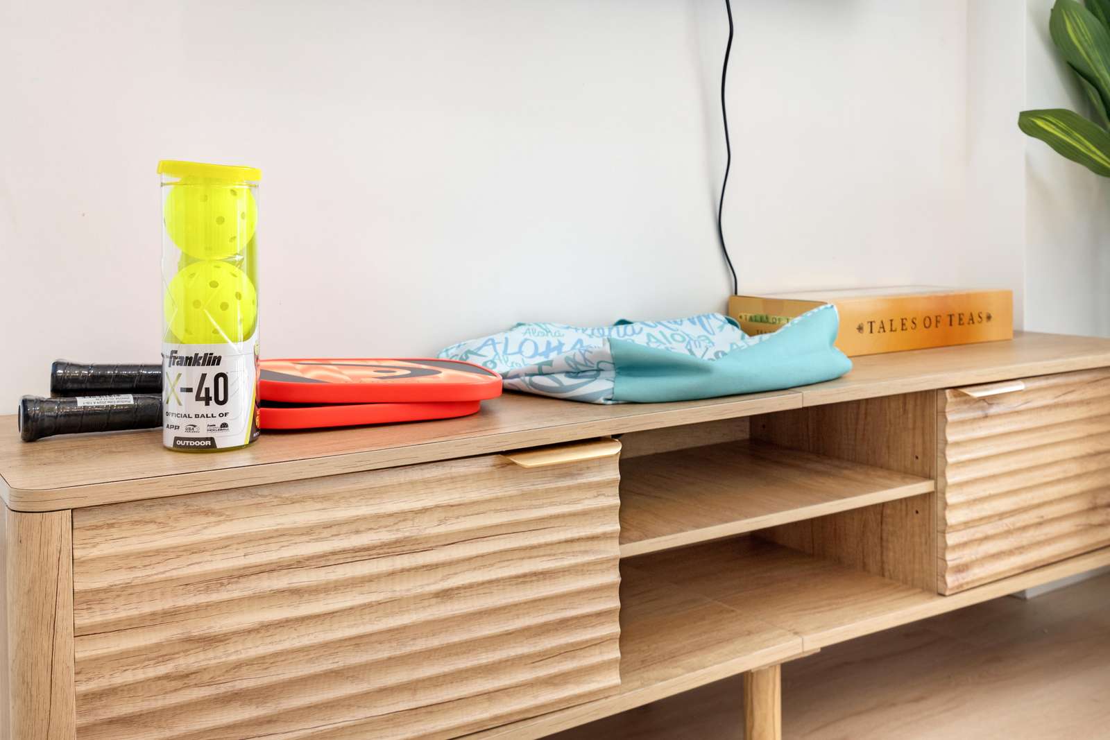 Light wood media console with textured sliding doors holds paddleball set, a book, and a folded cloth.