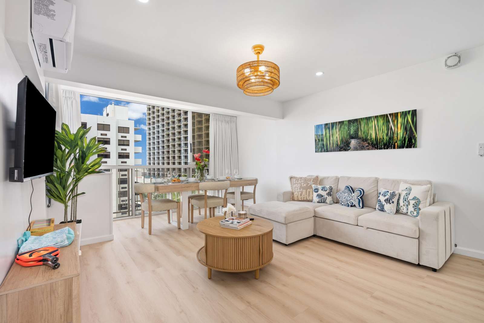 Round wood coffee table and cream sectional sofa with tropical-themed pillows beneath a bamboo woven light fixture.
