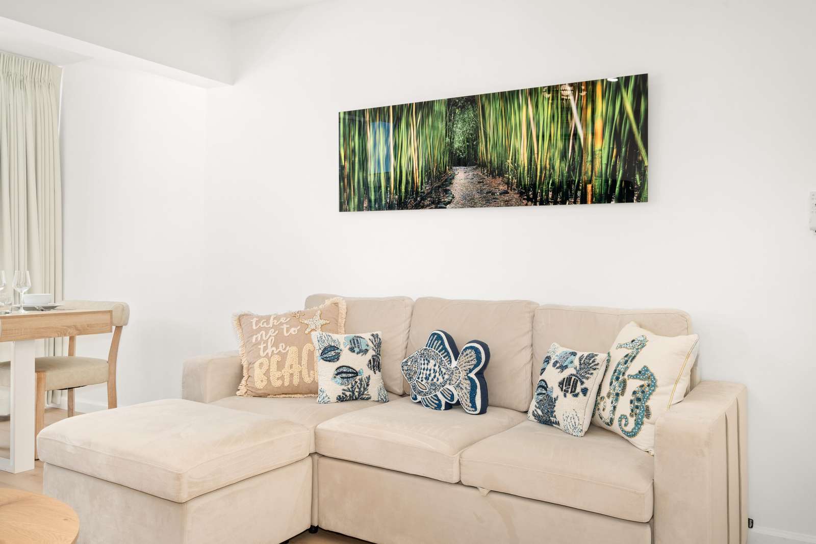 Light beige sectional sofa with ocean-themed throw pillows sits beneath a vibrant bamboo forest wall art.