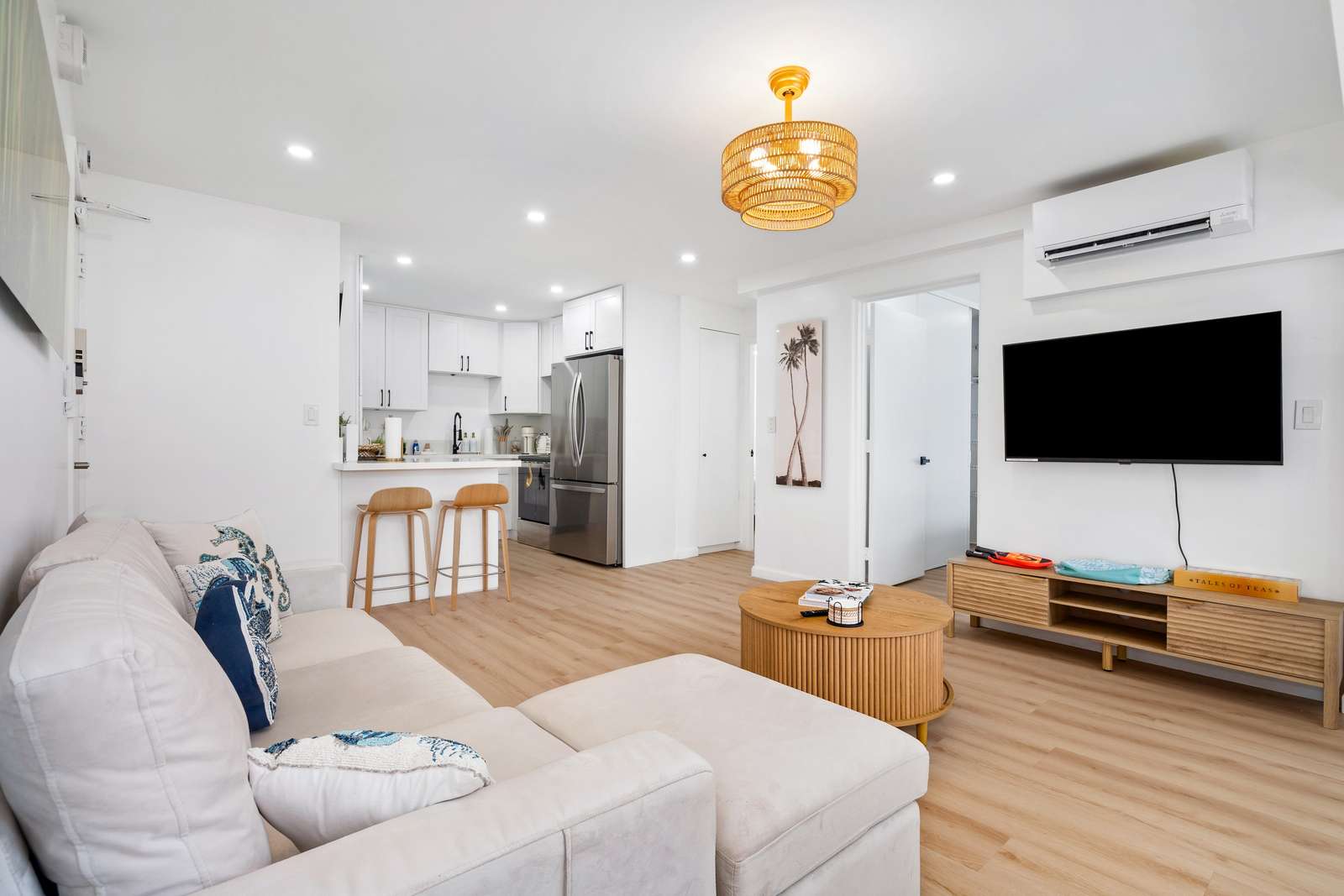 Rattan pendant light hangs from a white ceiling above the living area with light wood furniture and seamless flooring.
