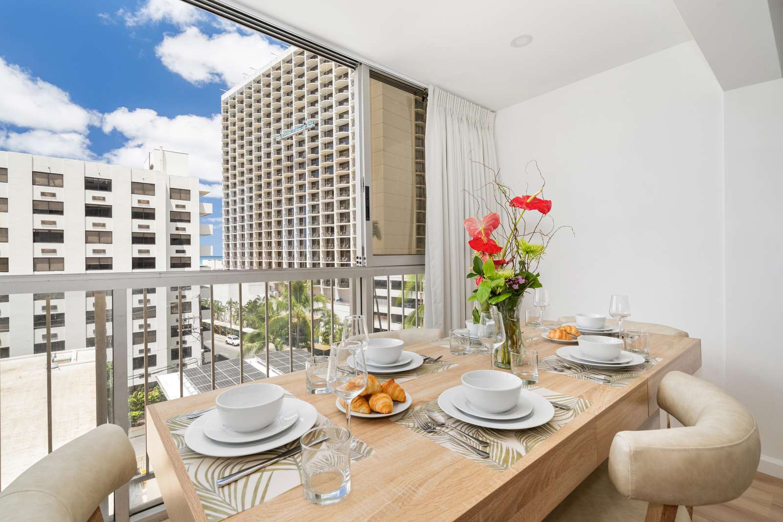 Natural light fills the dining area with a light wood table, neutral cushioned chairs, and red floral centerpiece.