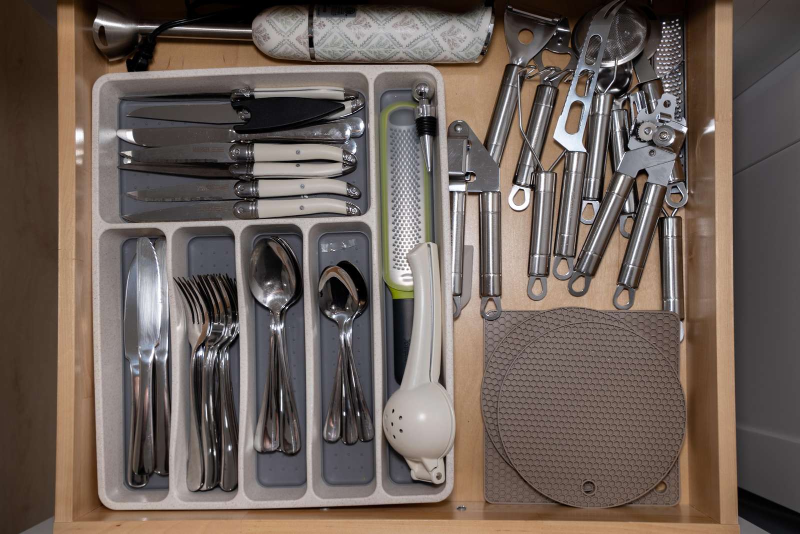 Organized kitchen drawer with stainless steel cutlery, white-handled knives, metal utensils, and silicone hot pads.