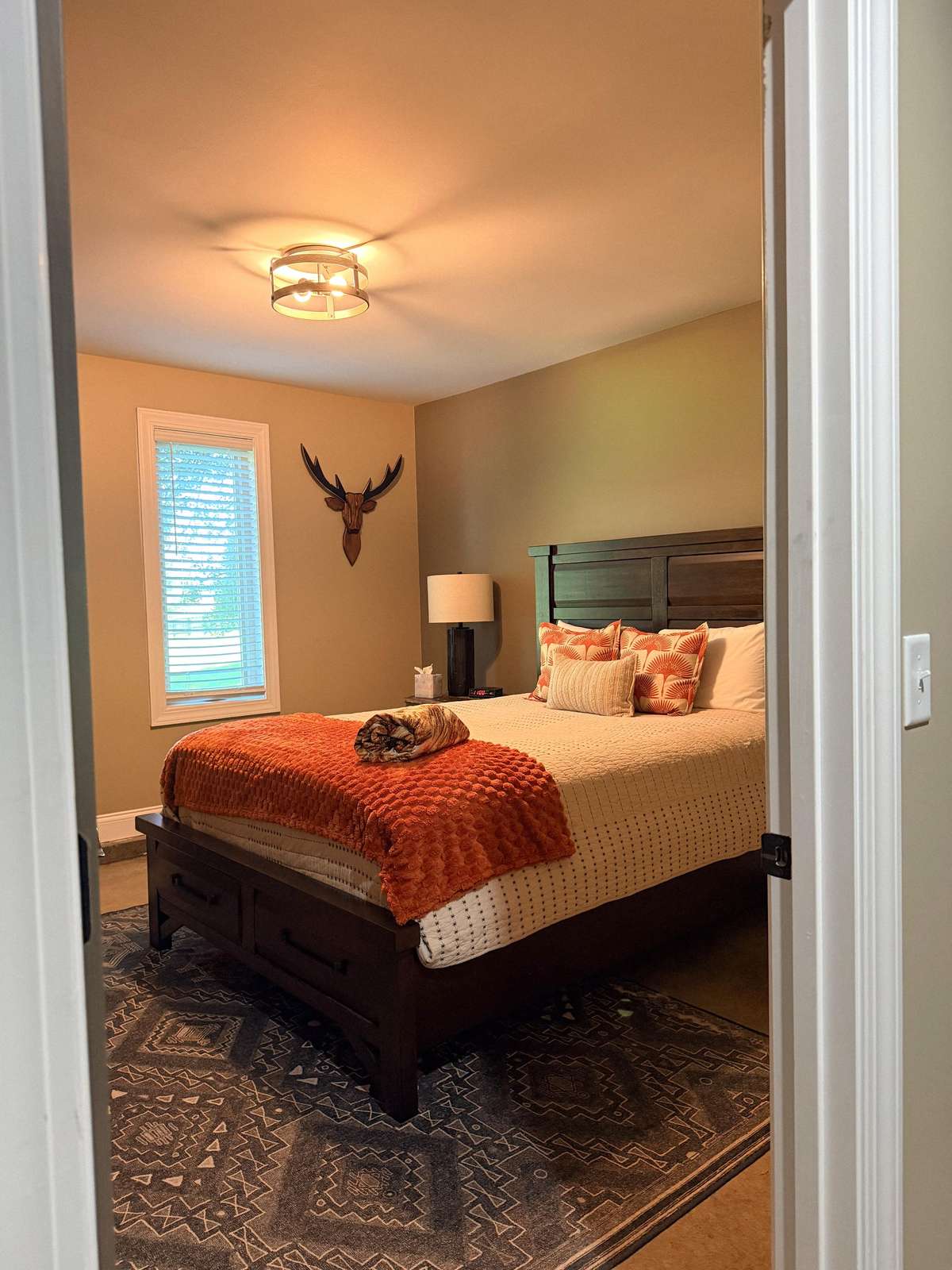 View into the bedroom featuring a dark wood bed with orange textured throw and patterned pillows on a geometric rug. - property