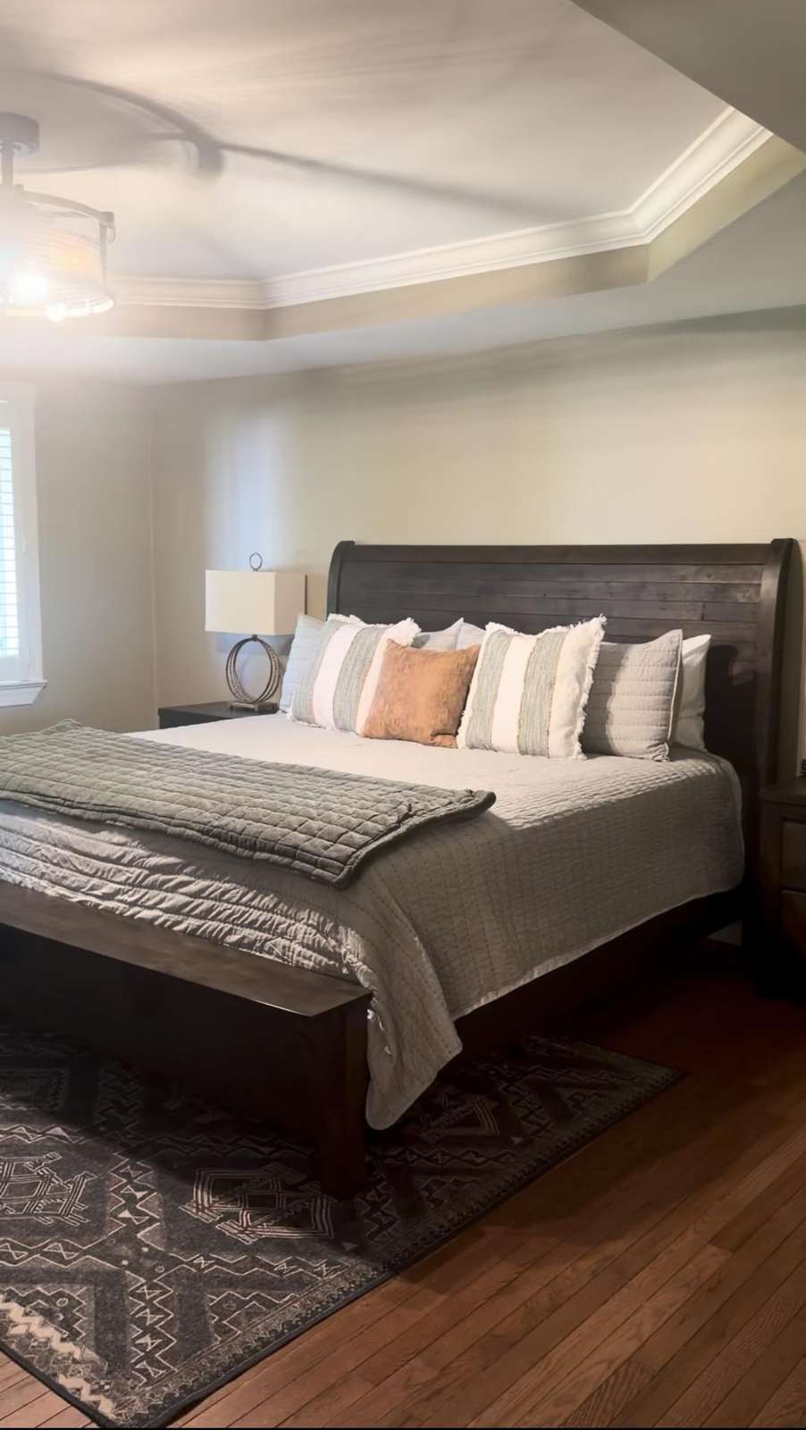 A dark wood sleigh bed with gray and white pillows sits atop a patterned rug on hardwood floors. - property