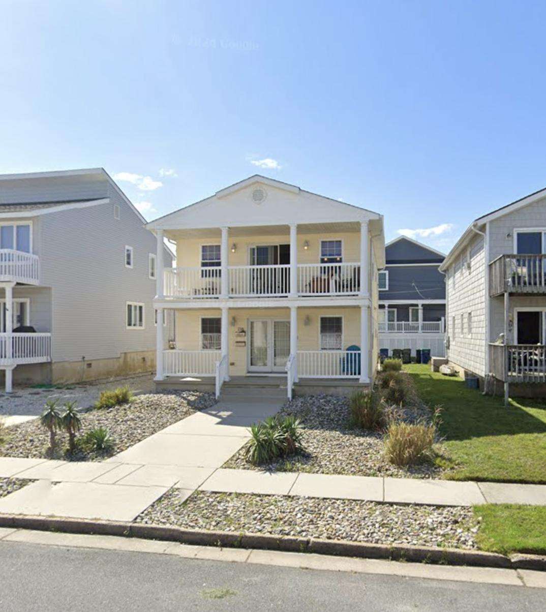 Front exterior of the two-story condo with double balconies, white railings, and a stone-lined front yard. - property