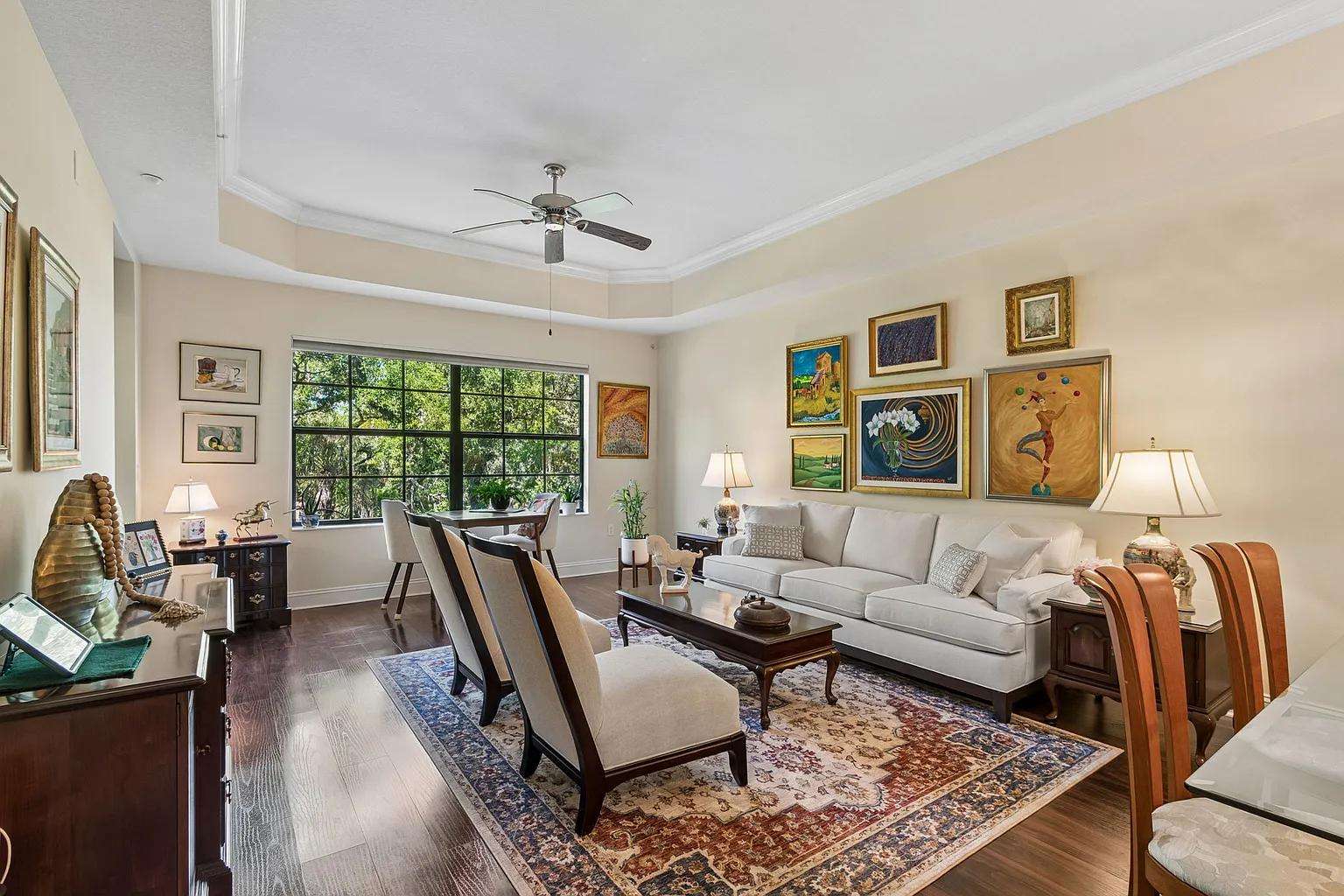 Living room with a cream sofa, dark wood coffee table, patterned area rug, and large window overlooking greenery. - property