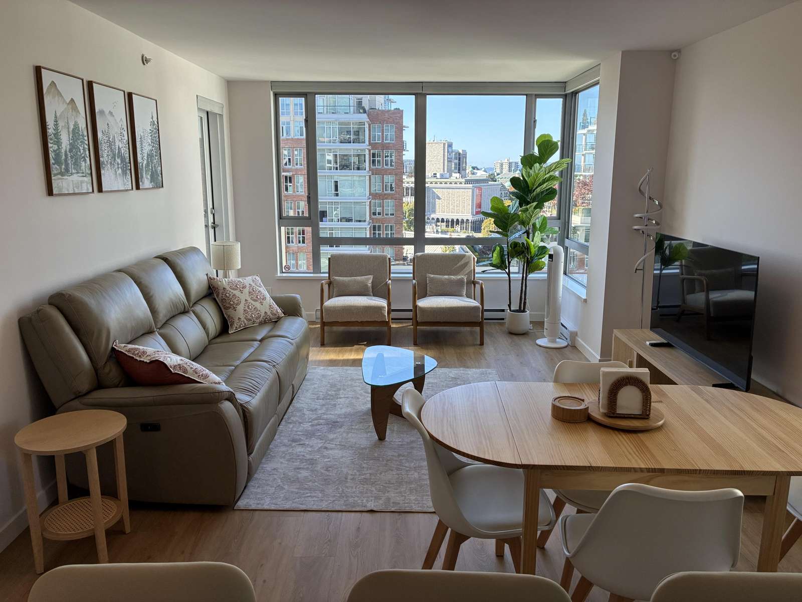 Natural light fills the living and dining area with light wood flooring, a round wood table, and a flat-screen TV on a low console. - property