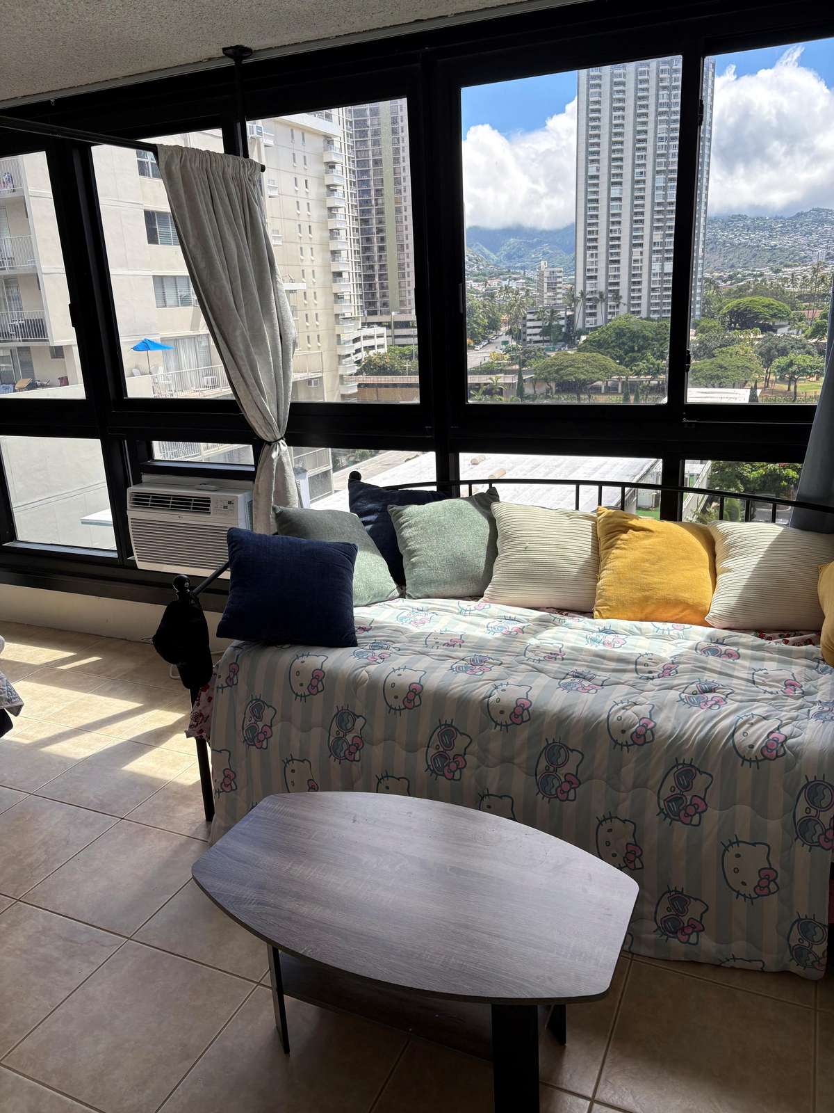 Daybed with colorful pillows and a cartoon-patterned quilt sits beneath large windows showing city and mountain views. - property
