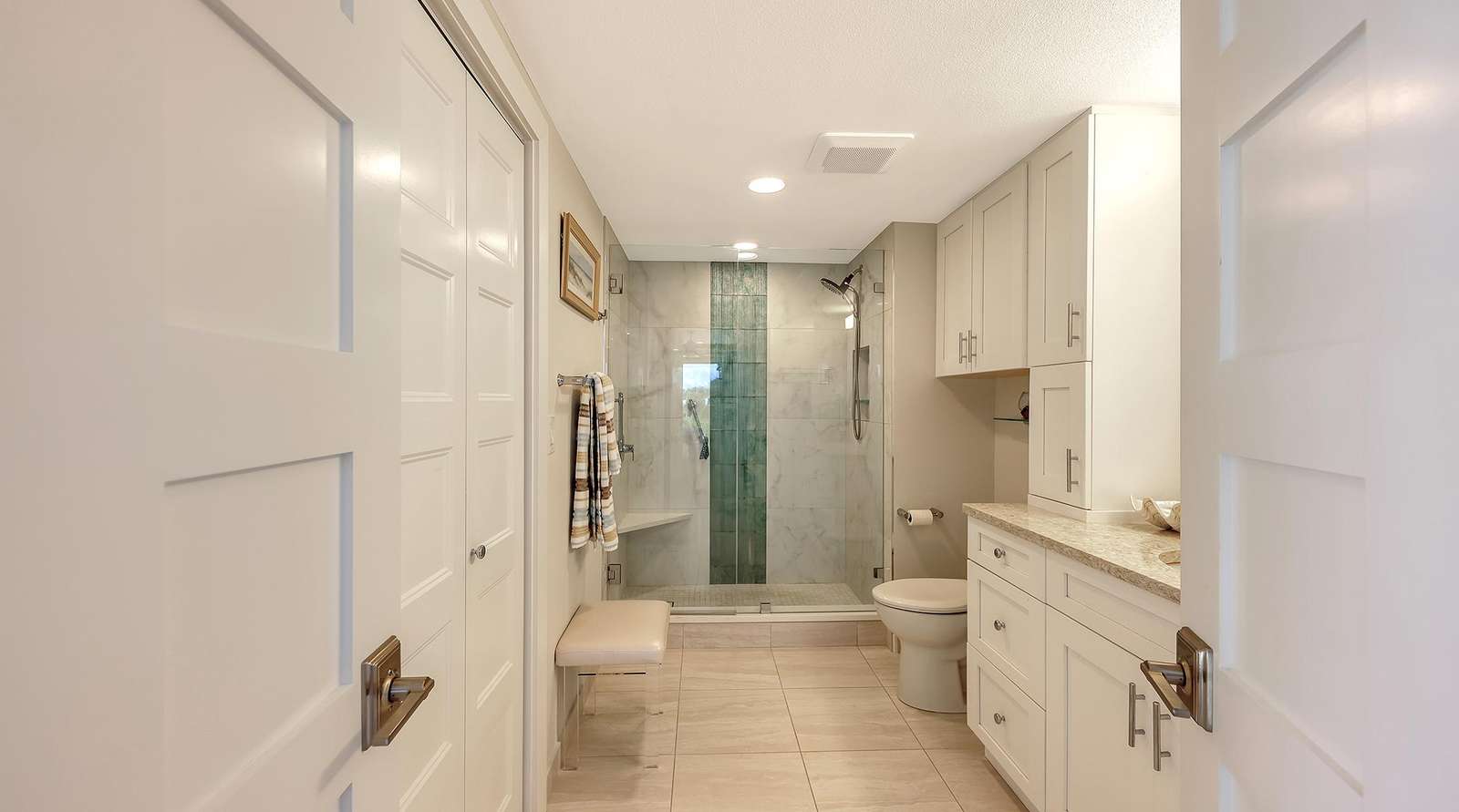 Bathroom with glass-enclosed shower featuring green tile accent, beige floor tiles, and white cabinetry.