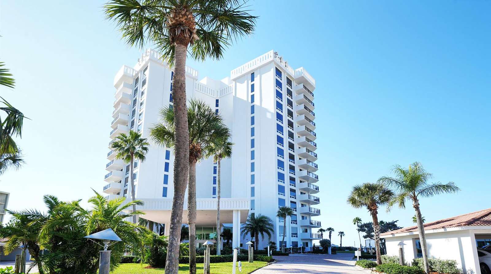 White high-rise condo building with balconies and palm trees under a clear blue sky.