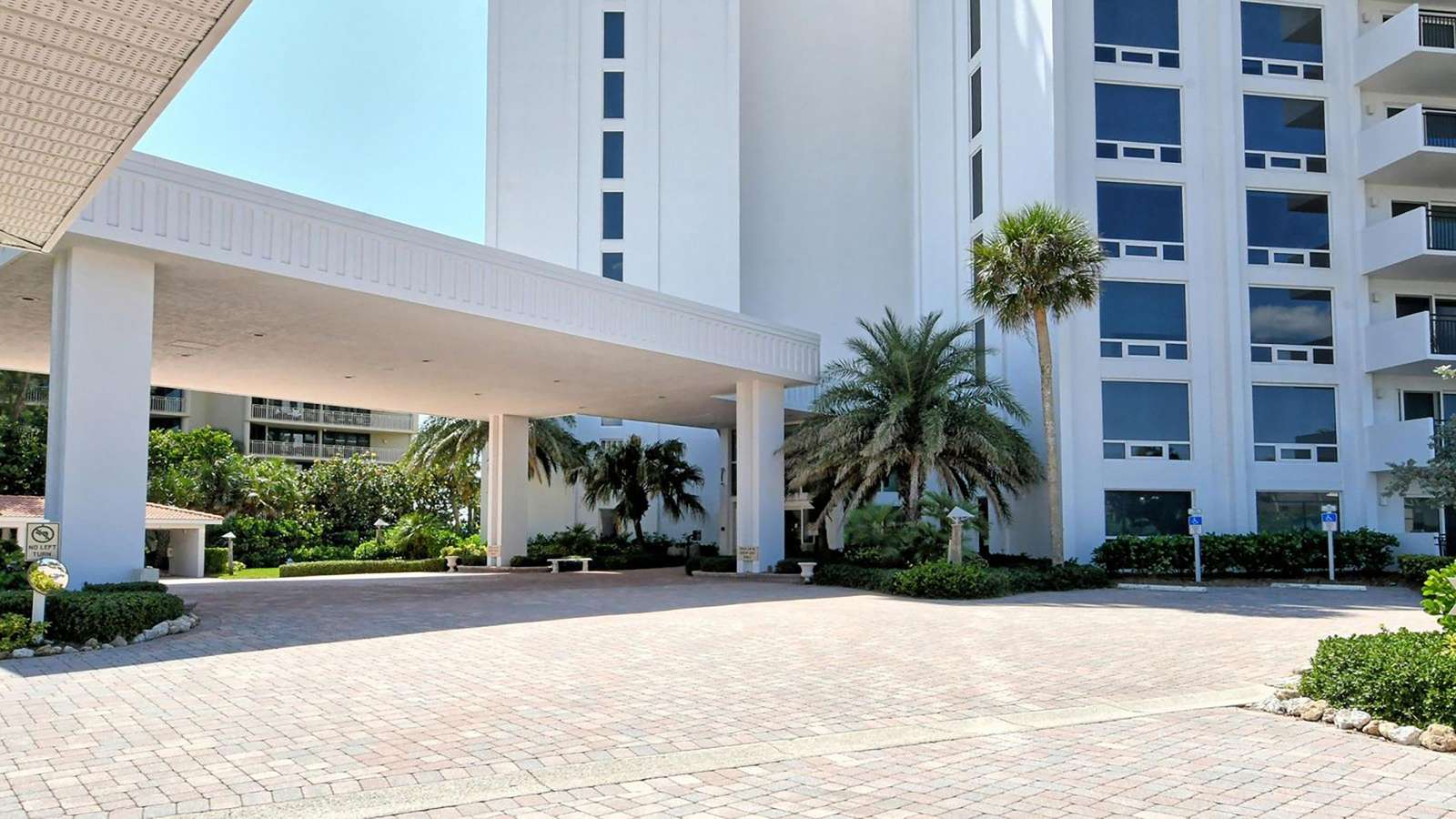 Paved driveway and covered entrance framed by white stucco columns and tropical palm trees.