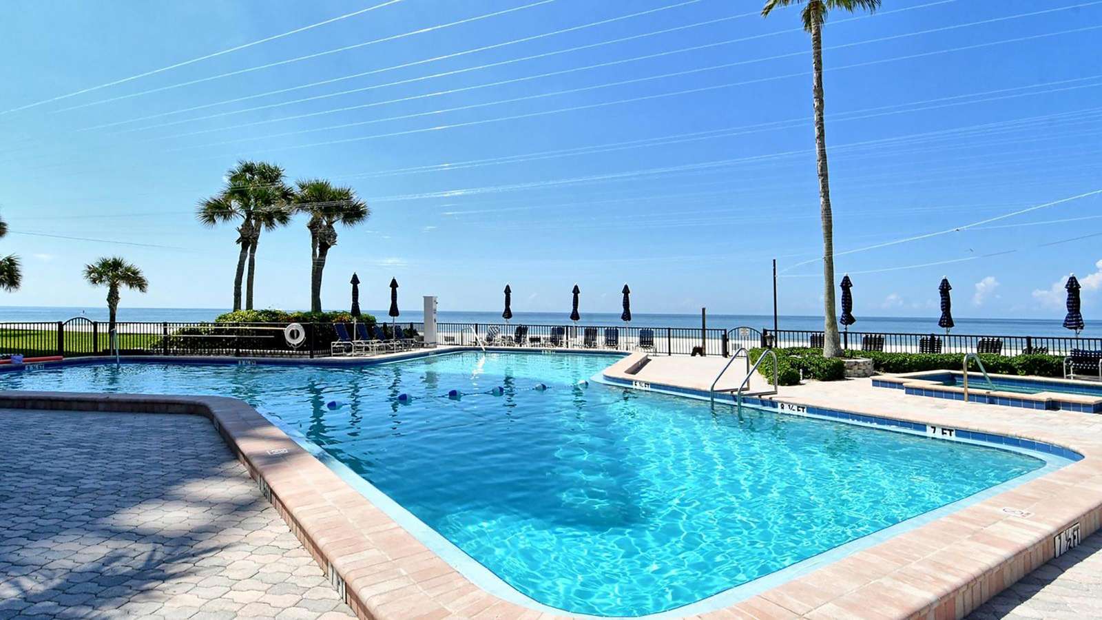 Outdoor pool with clear blue water, surrounded by a brick deck and palm trees, overlooking the ocean.