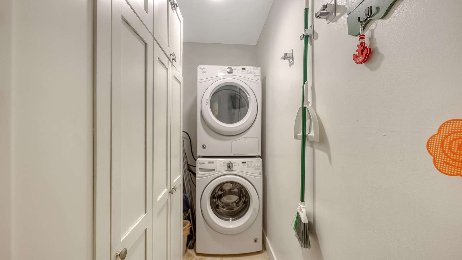 Laundry area with stacked white washer and dryer, beige tile floor, and white paneled storage cabinets.