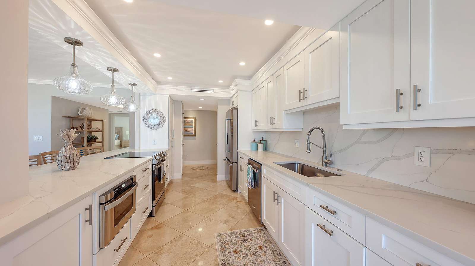 Galley kitchen with white shaker cabinets, marble countertops, stainless steel appliances, and recessed lighting.