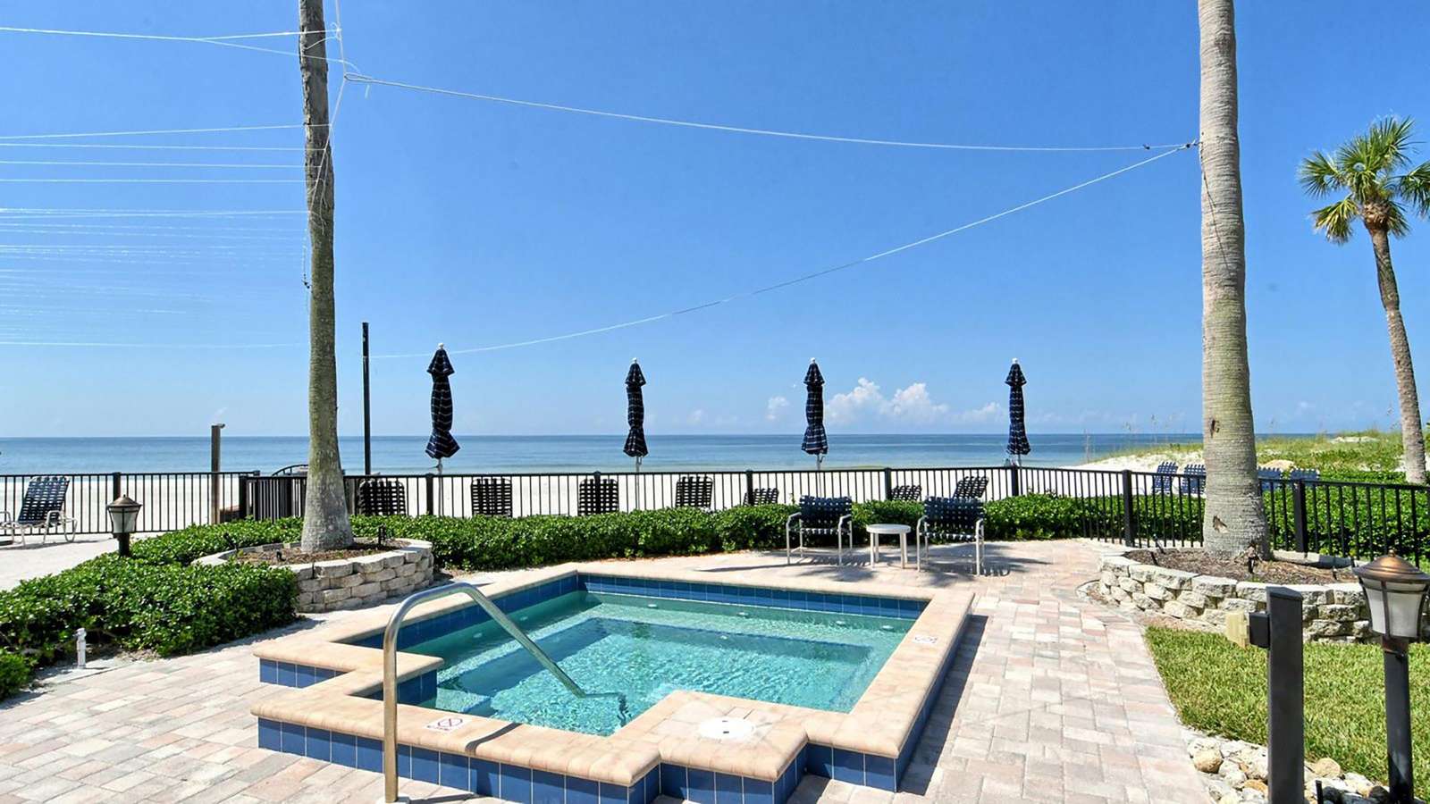 Beachfront hot tub with tiled edges, surrounded by palm trees, lounge chairs, and umbrellas against ocean views.