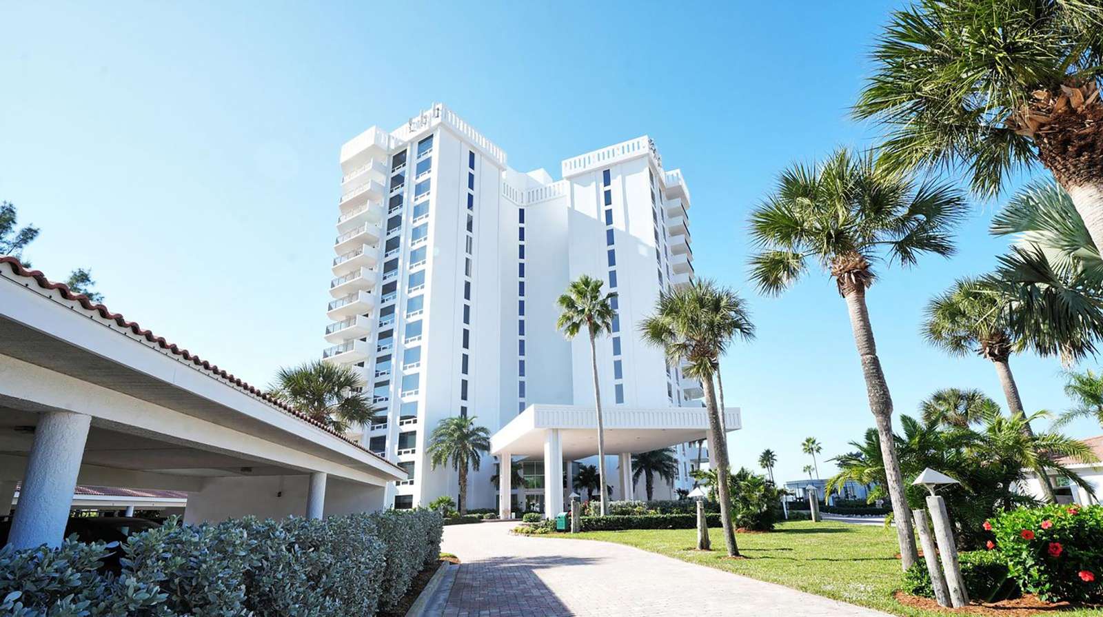 Exterior view of the Islands West high-rise condo building framed by palm trees under a clear blue sky.