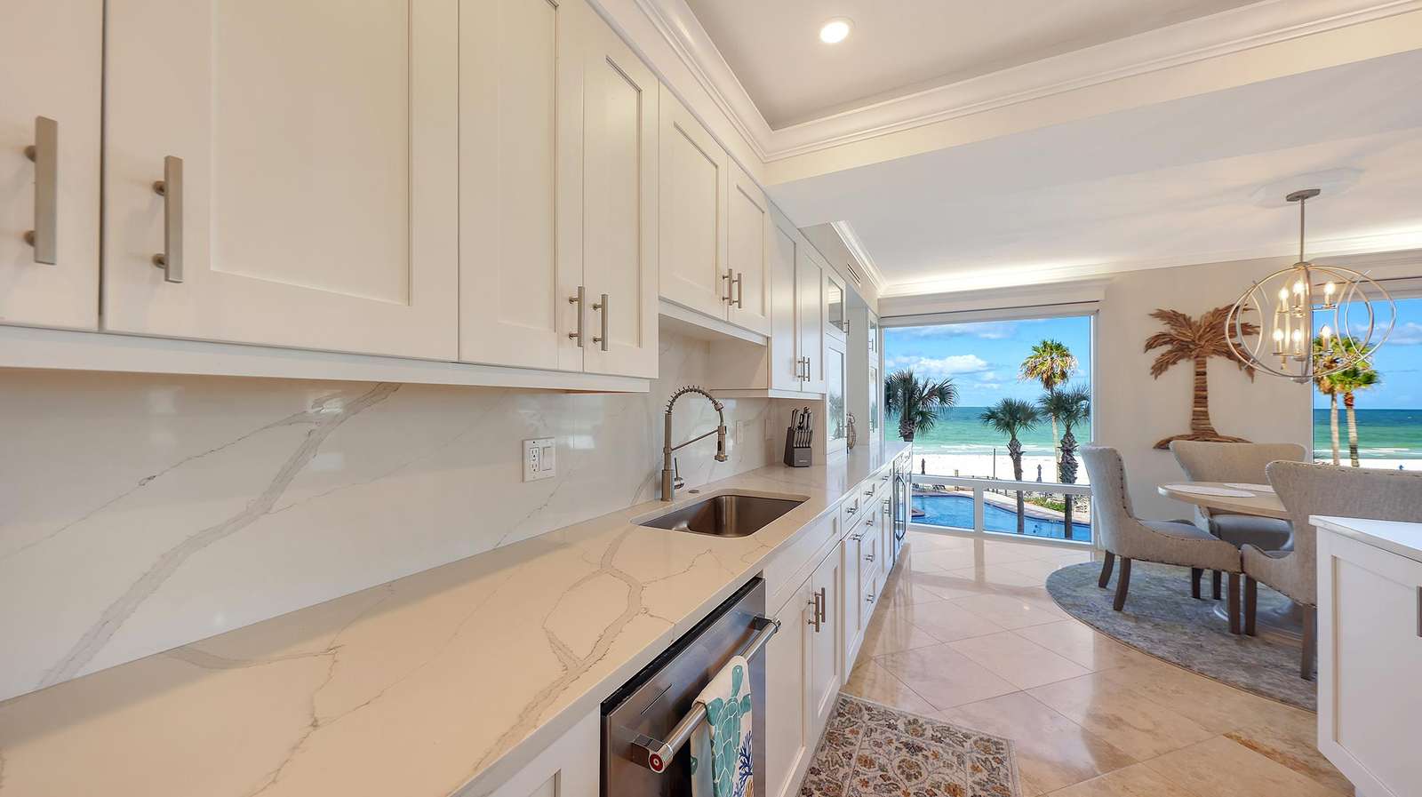 White shaker cabinets and marble countertops line the kitchen, opening to a dining area with ocean views.