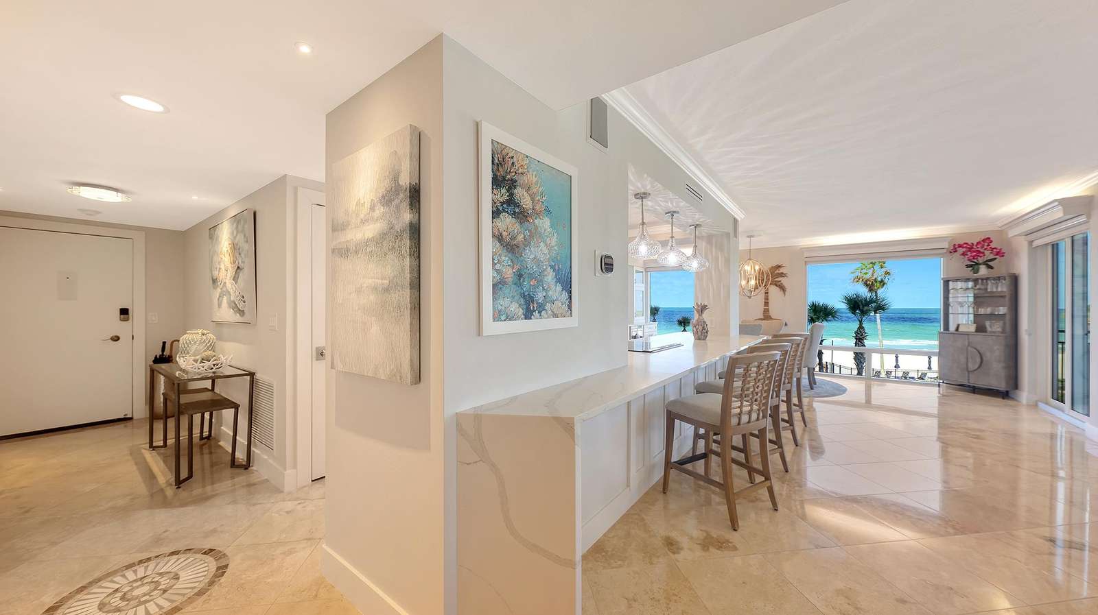 Marble tile floors extend through the open living room and bar area with glass pendant lights and ocean views.