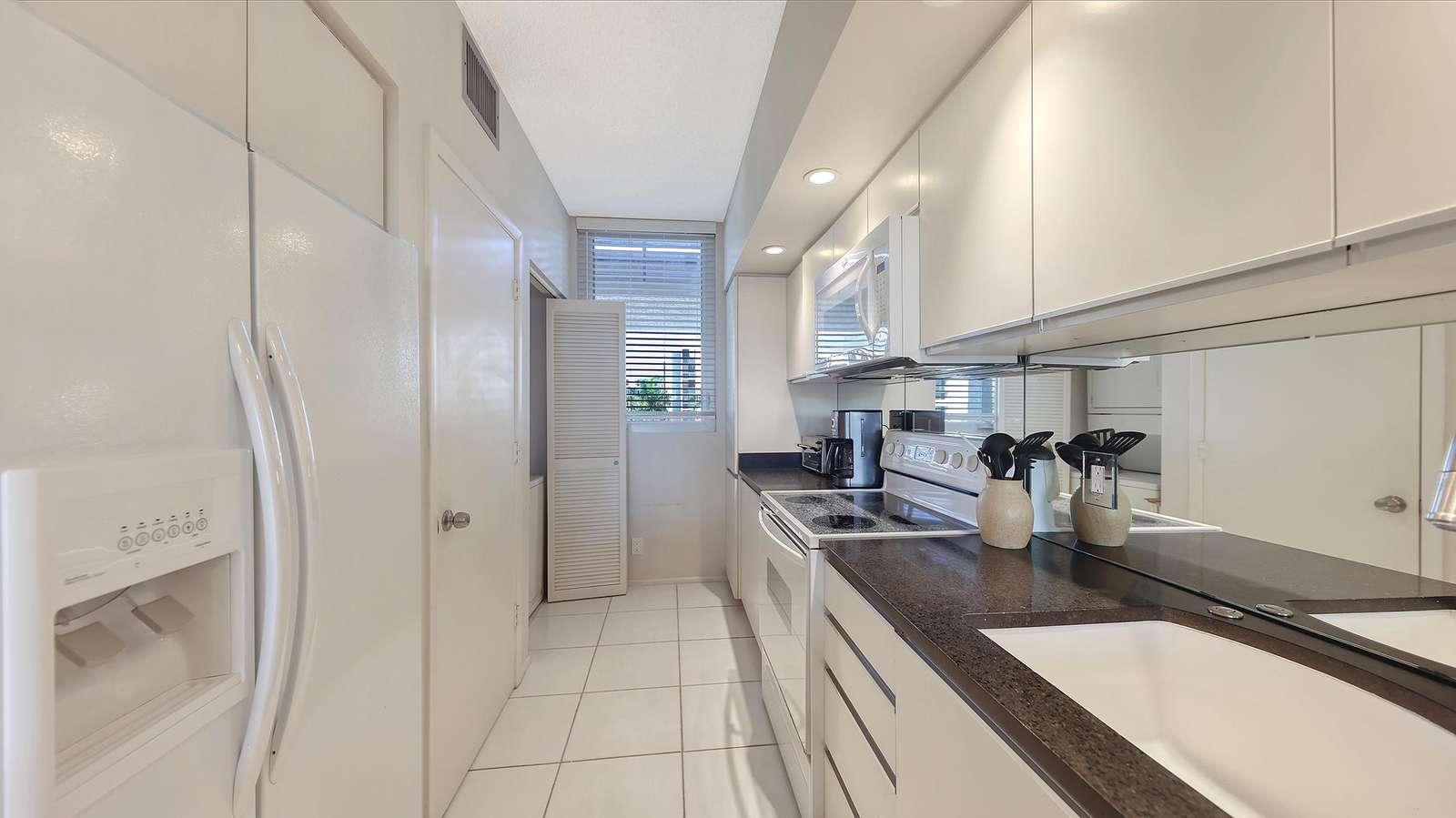 Galley kitchen with white cabinetry, black granite countertops, and a mirrored backsplash.