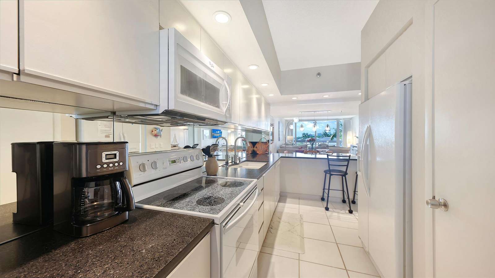 Black granite countertops contrast with white cabinetry in the kitchen, featuring a coffee maker and electric stove.