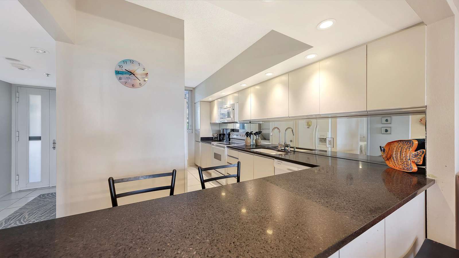 Dark granite countertop wraps around the kitchen bar with black metal stools and white cabinetry above.