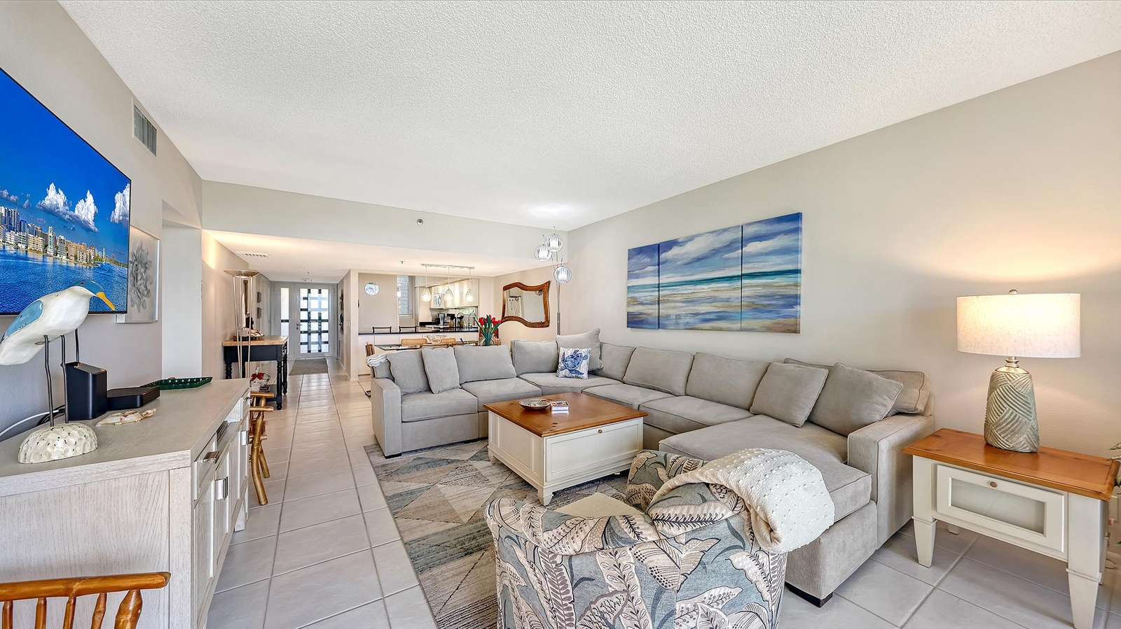 Light gray sectional and patterned armchair surround a wood-topped coffee table on a geometric rug.