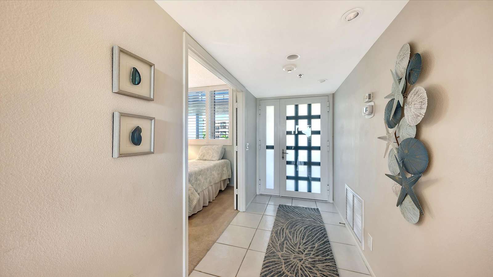 Entryway with white tiled floor, patterned runner, glass-paneled door, and coastal-themed wall art.