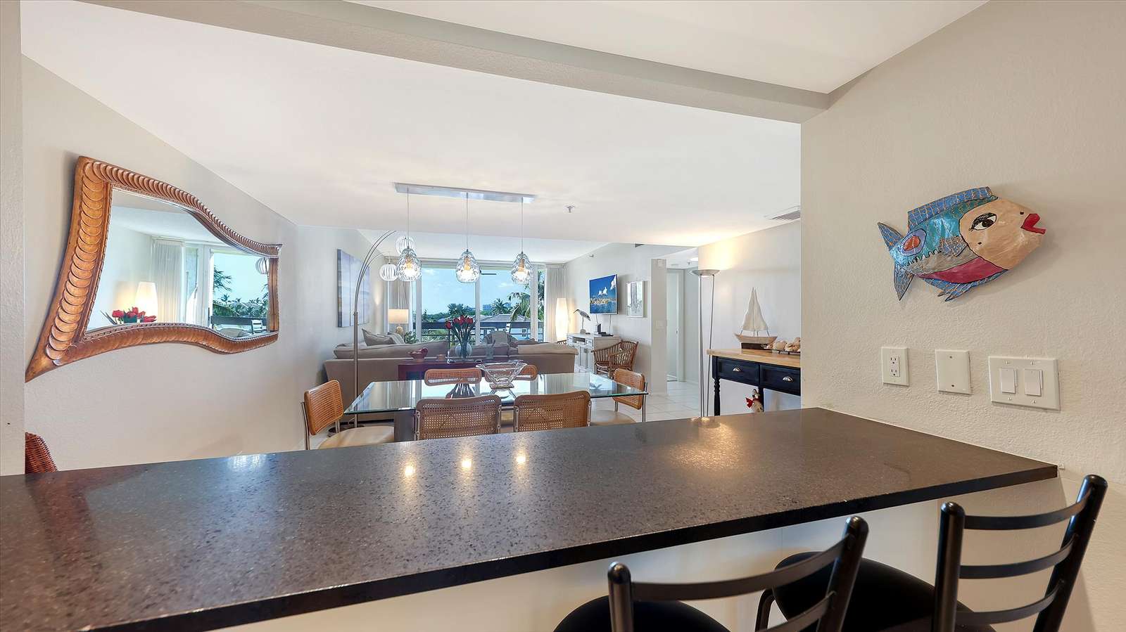 Black granite breakfast bar with two stools overlooks dining area and living room with balcony view.