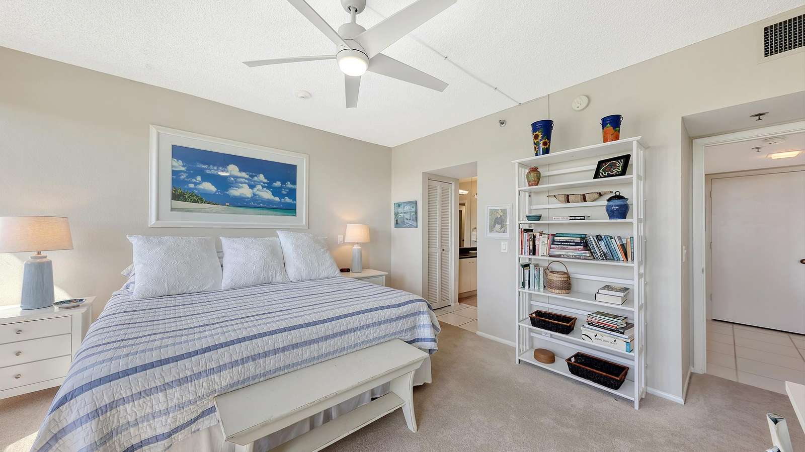 King bed with a striped quilt and white pillows, flanked by twin nightstands and lamps in the bedroom.