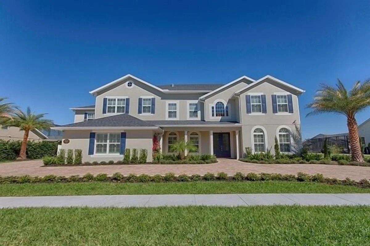 Two-story villa with beige stucco, dark shutters, arched windows, and palm trees on a brick driveway. - property