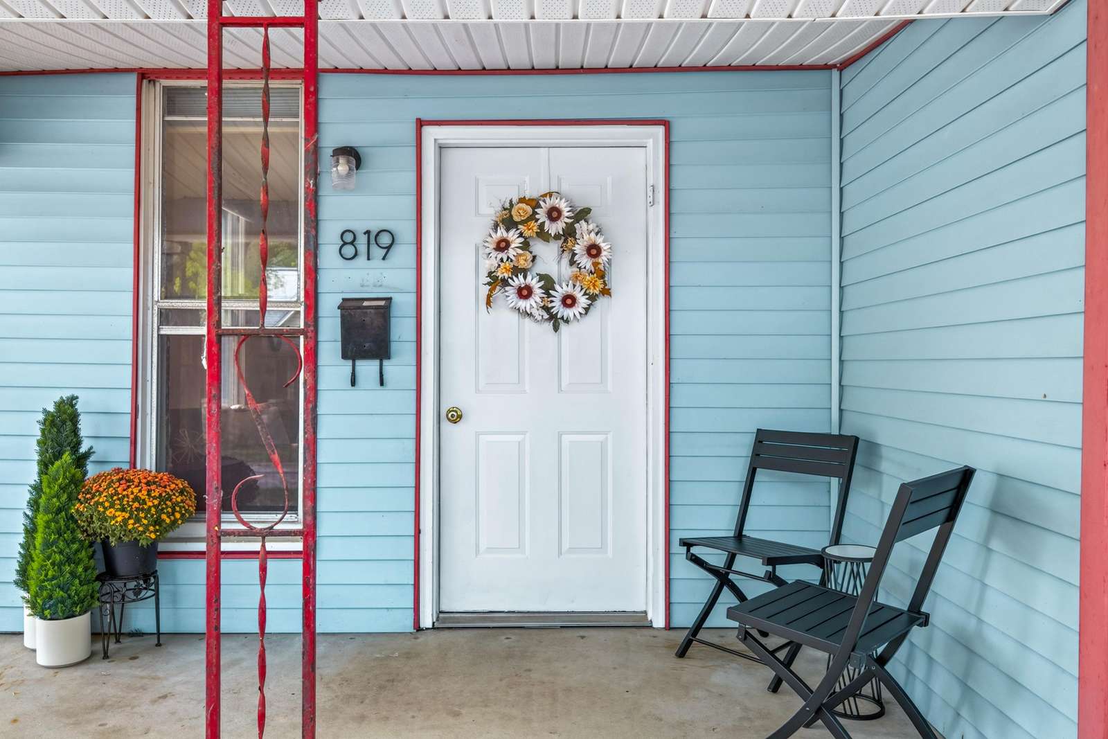 Front porch with pale blue siding, white door decorated with a floral wreath, and black folding chairs. - property