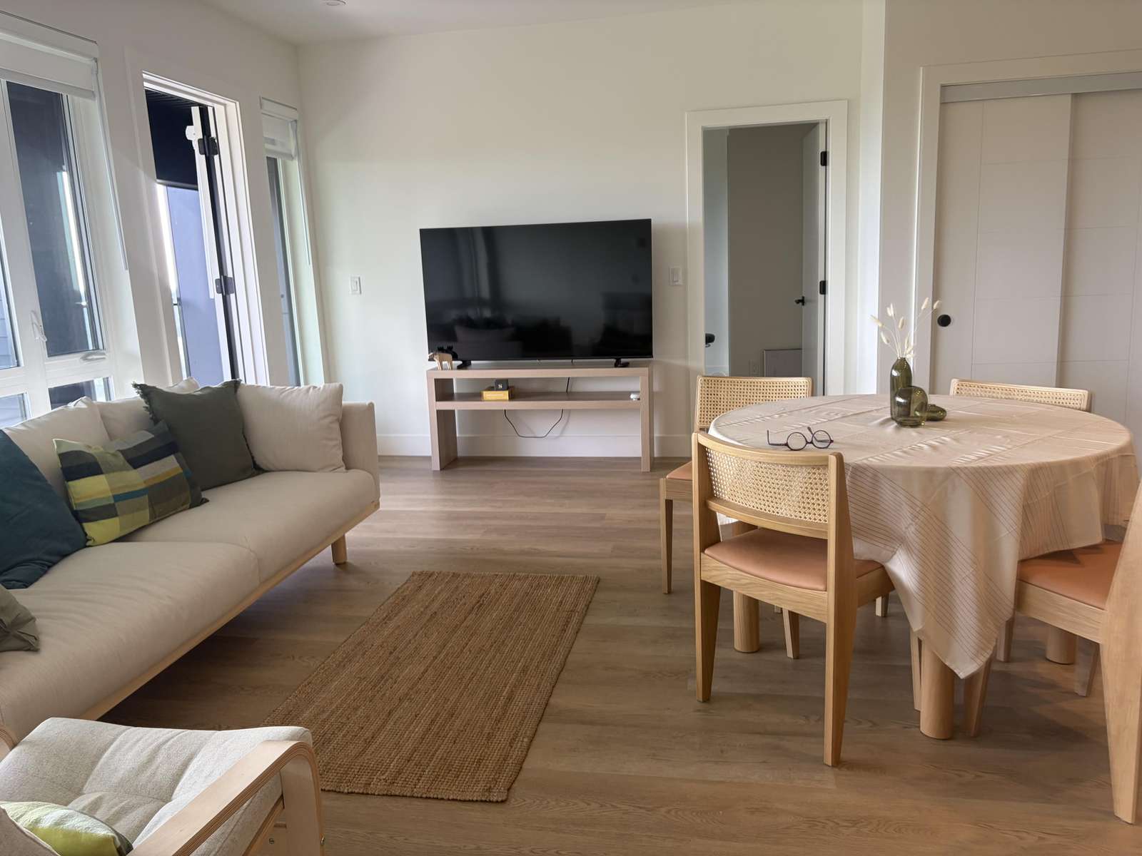 The living and dining area features light wood floors, a beige sofa with colorful cushions, and a round table with woven chairs. - property