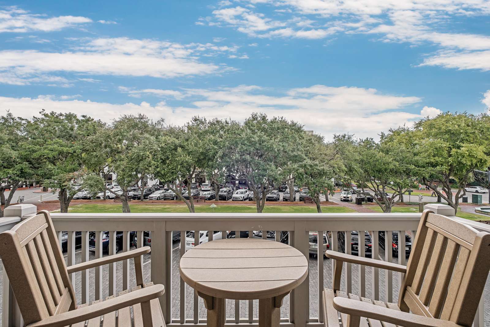 Balcony with two wooden armchairs and a round table overlooks leafy trees and a brick-paved parking area. - property