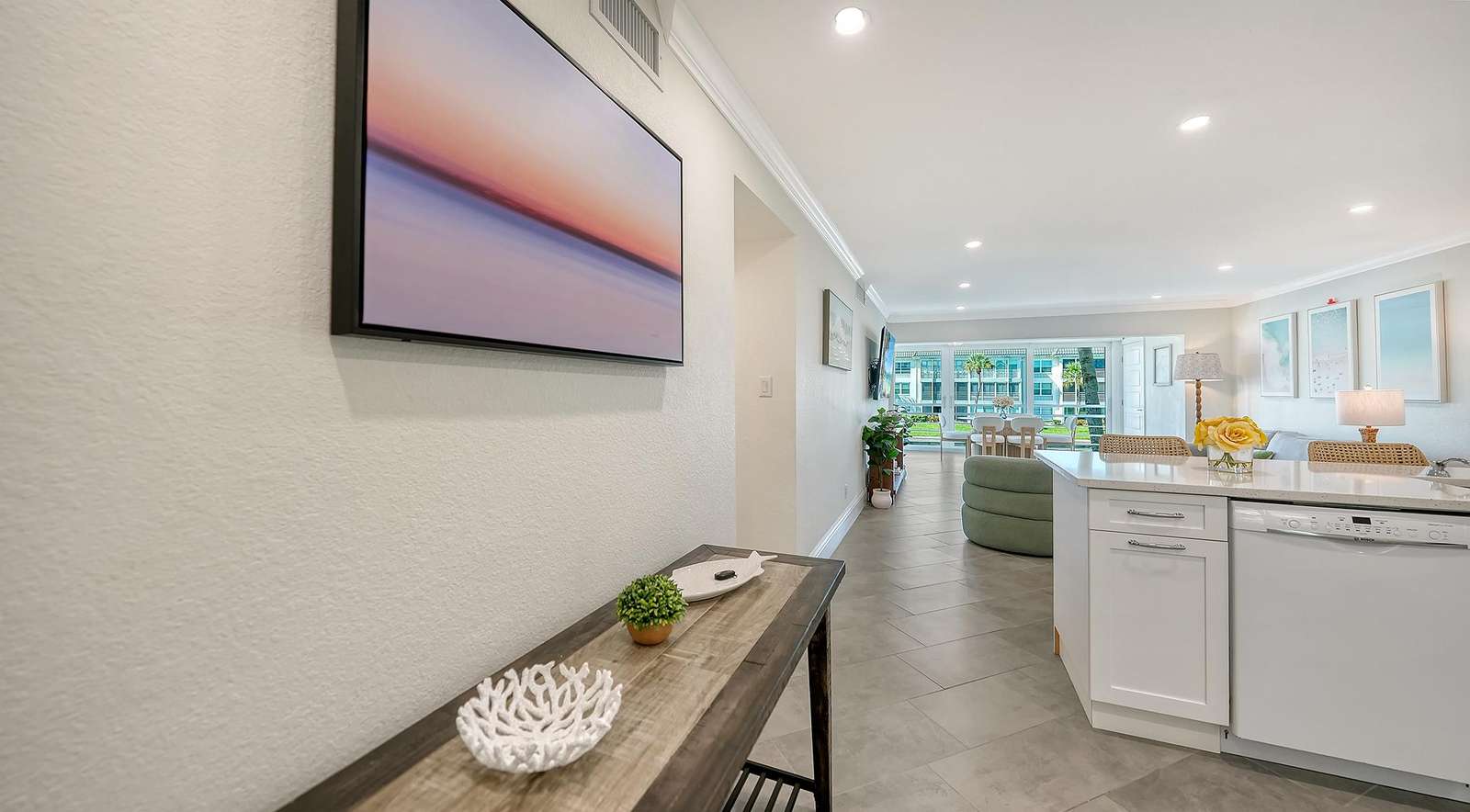 Entryway console table with decorative accents leads toward open living area and kitchen with white cabinetry.
