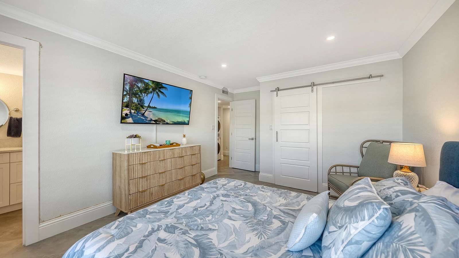 Primary Bedroom featuring a patterned blue-gray bedspread, wooden dresser, wall-mounted TV, and sliding barn door closet.