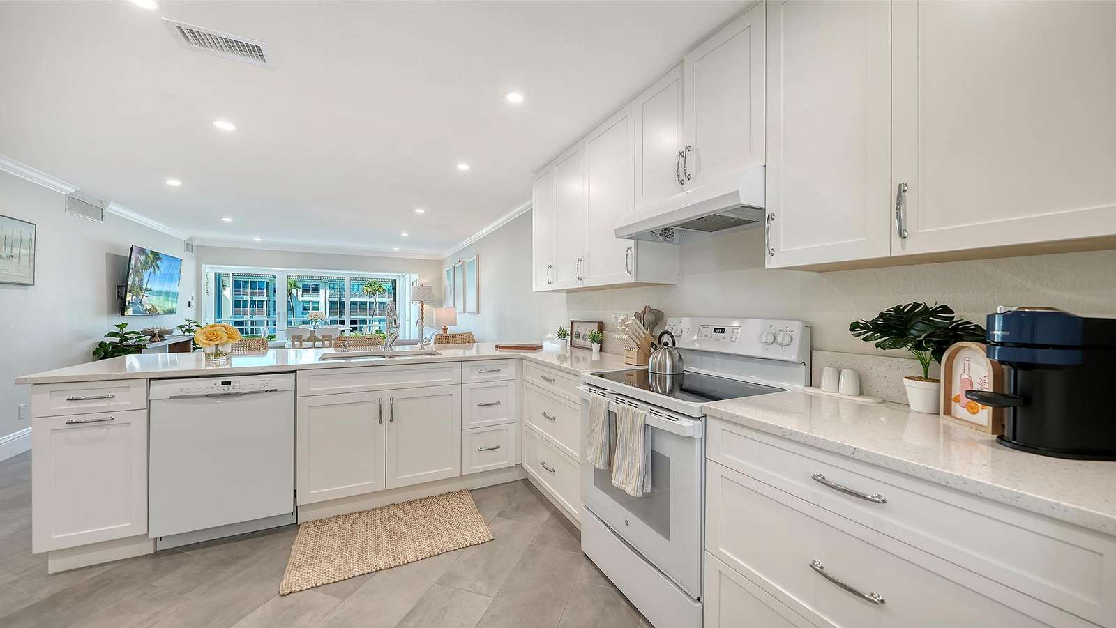 White cabinetry and quartz countertops surround a white electric stove and built-in dishwasher in the kitchen.