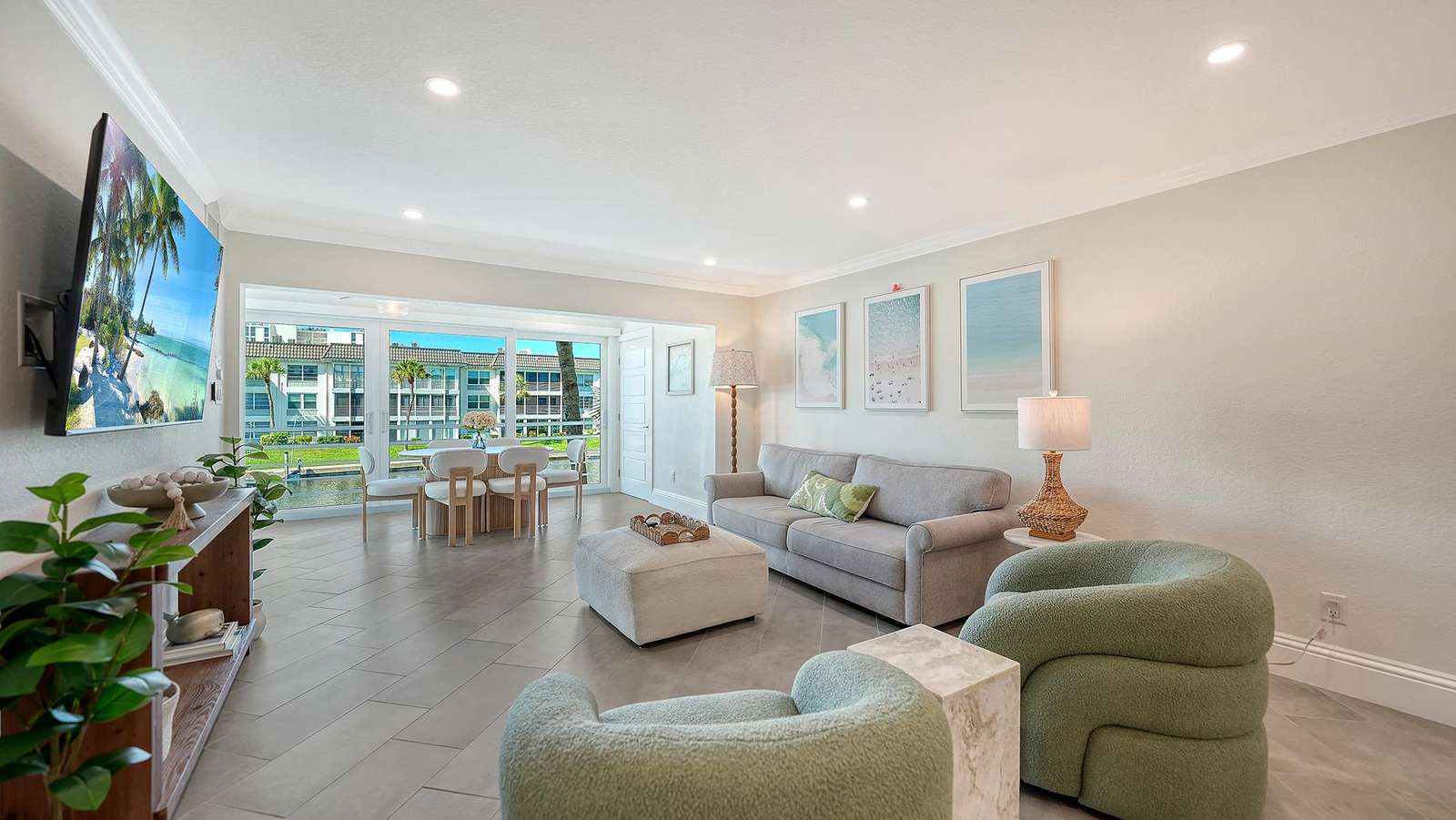 Living room with pale gray sofa, green boucle chairs, tiled floors, and waterfront views through sliding glass doors.