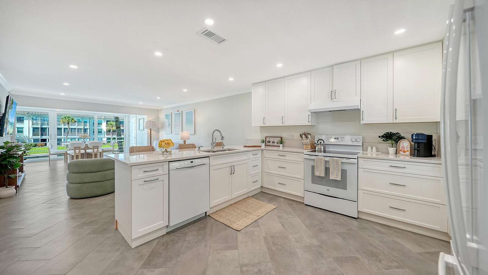 White shaker cabinets and quartz countertops frame the kitchen with herringbone tile flooring and open living room views.