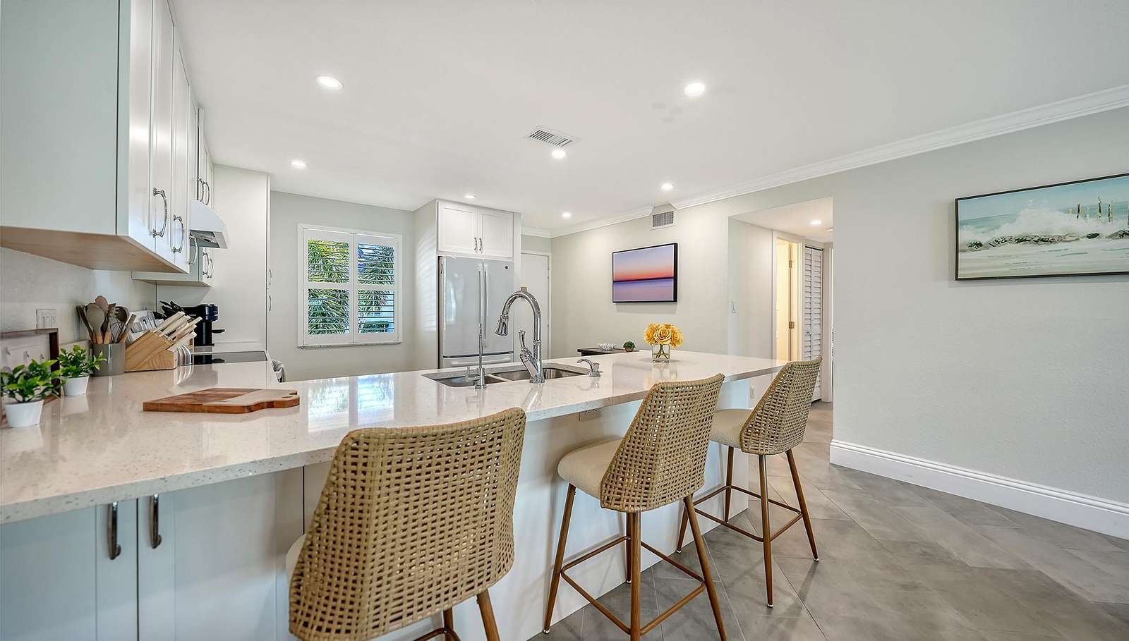 Quartz countertop stretches across the kitchen island with three woven back bar stools and under-cabinet lighting.