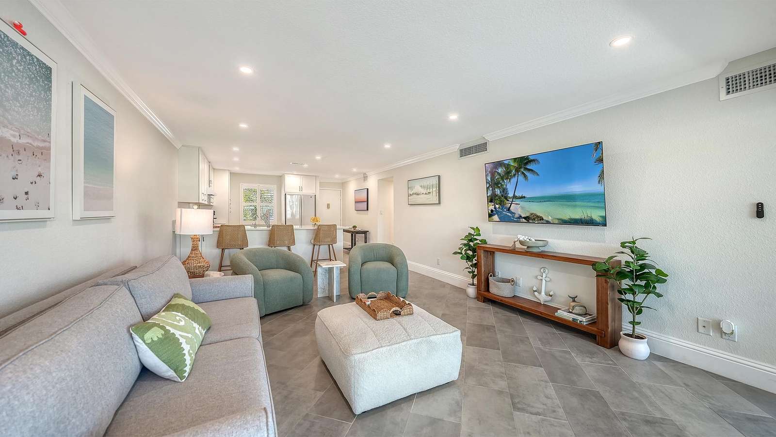 Living room with gray sofa, two sage armchairs, plush ottoman, and wall-mounted flat-screen TV.