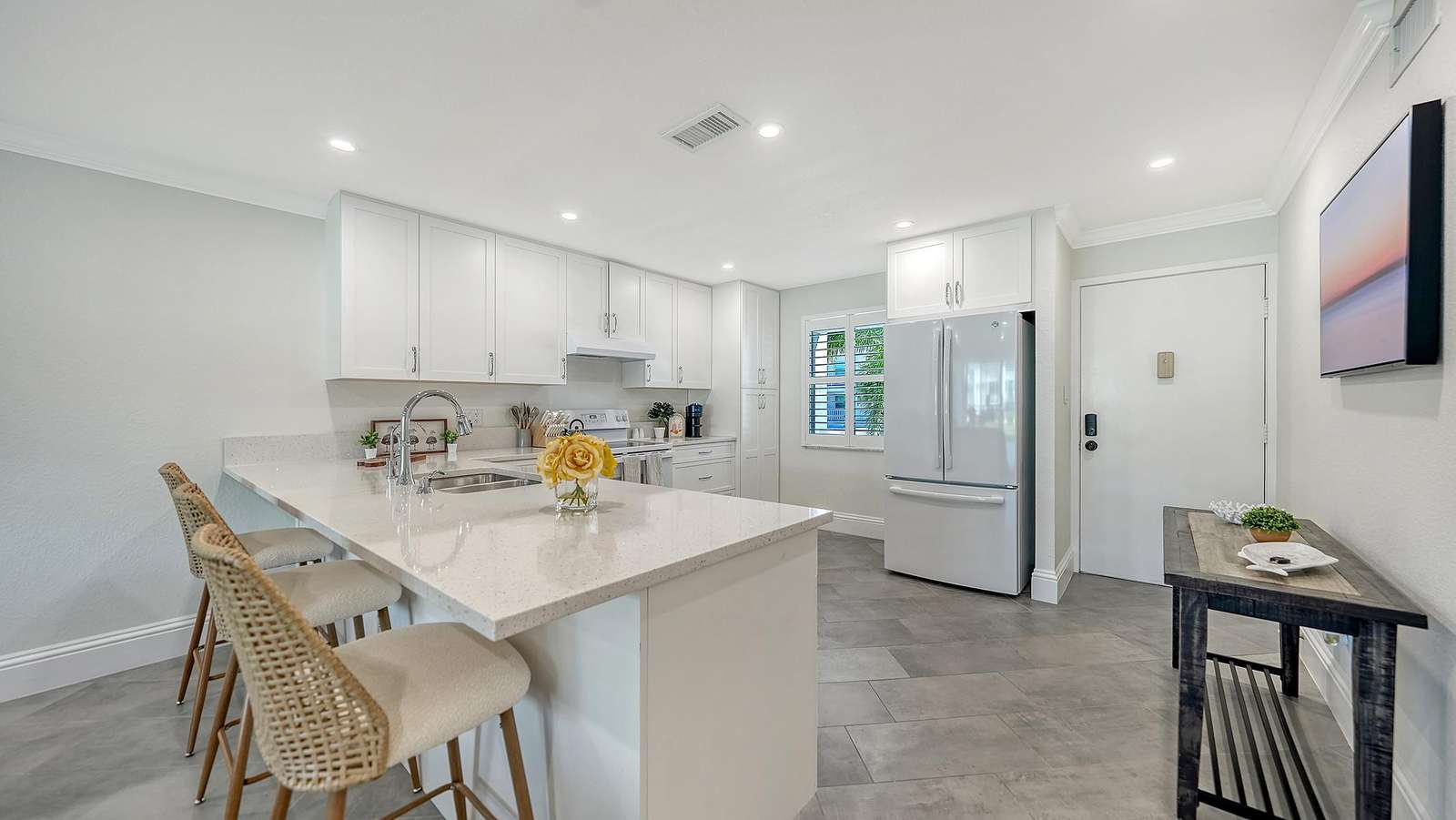 White quartz countertops extend into a breakfast bar with woven rattan stools and a stainless steel sink.