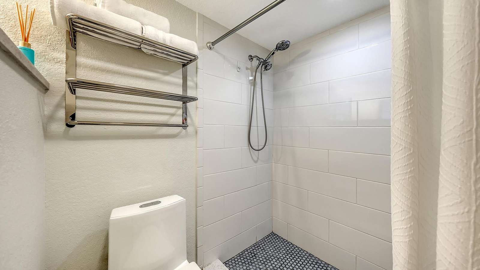 Bathroom shower features white subway tiles, a chrome handheld showerhead, and blue penny tile flooring.