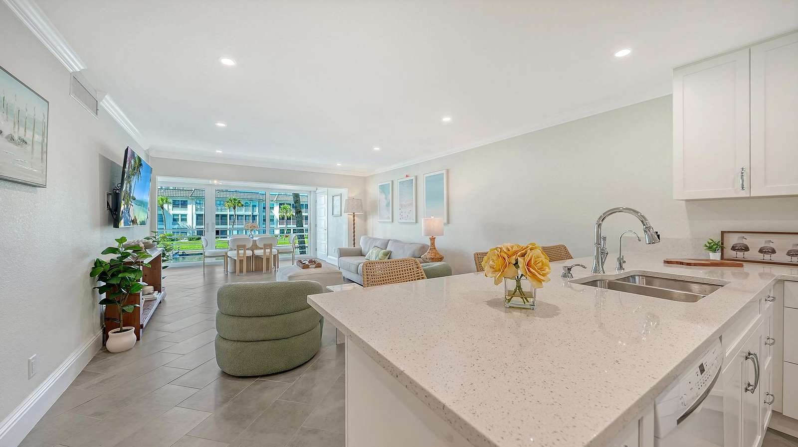 White quartz kitchen island with chrome fixtures overlooks light gray tiled living area and patio doors.